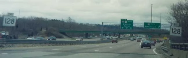 Route 128 highway sign in Massachusetts, surrounded by cars and trees